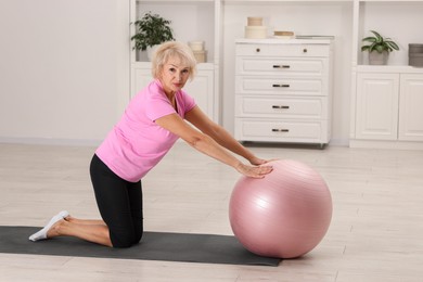 Photo of Senior woman exercising with fitness mat and ball at home