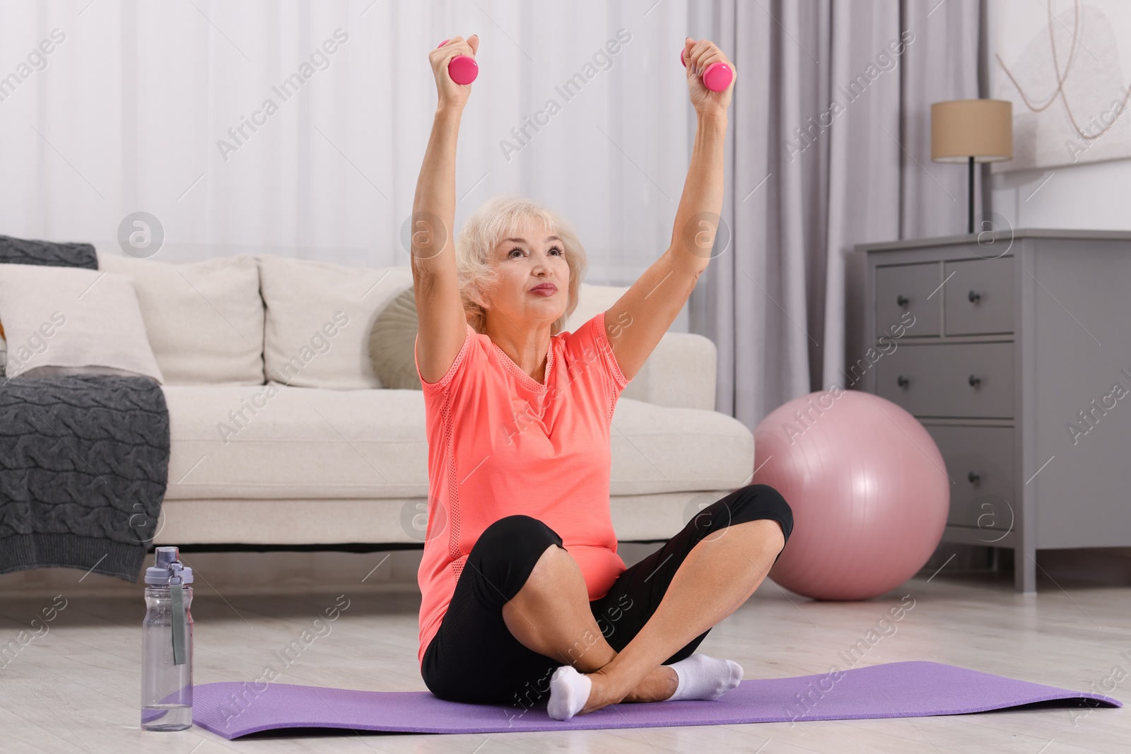 Photo of Senior woman exercising with fitness mat and dumbbells at home