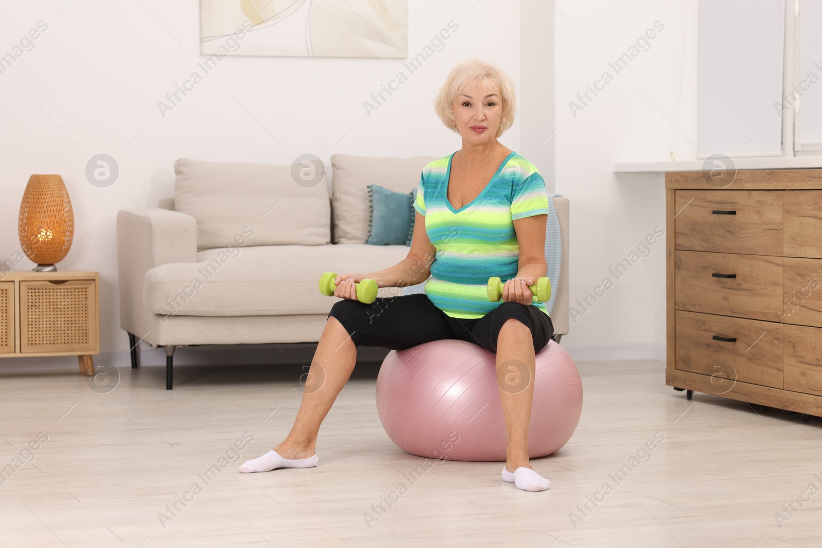 Photo of Senior woman exercising with fitness ball and dumbbells at home