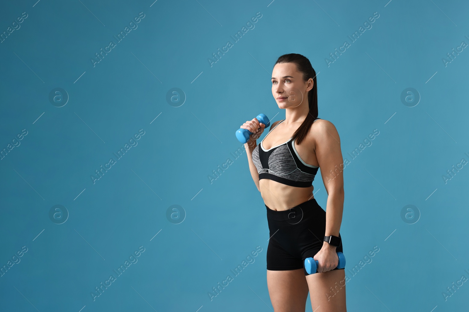 Photo of Woman in gym clothes exercising with dumbbells on light blue background, space for text