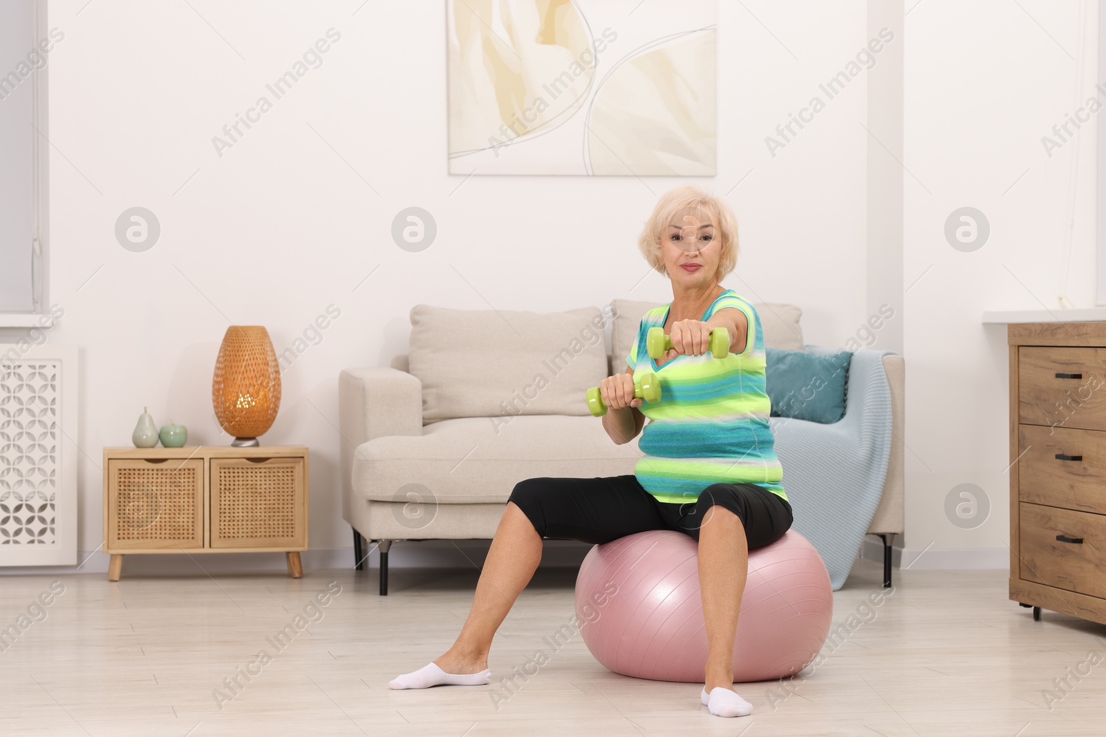 Photo of Senior woman exercising with fitness ball and dumbbells at home, space for text