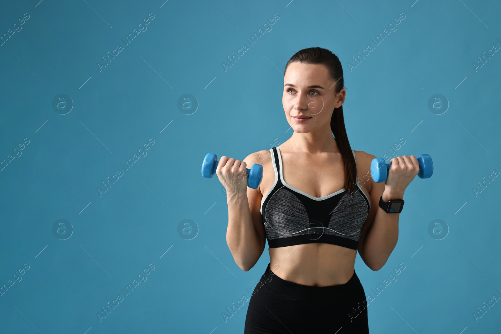 Photo of Woman in gym clothes exercising with dumbbells on light blue background