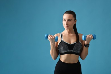 Photo of Woman in gym clothes exercising with dumbbells on light blue background