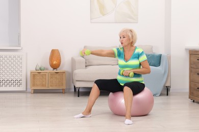 Photo of Senior woman exercising with fitness ball and dumbbells at home, space for text