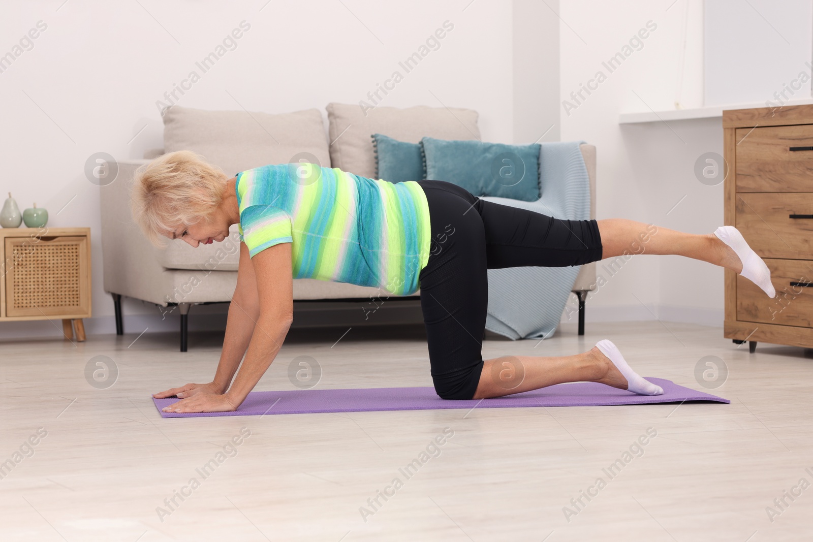 Photo of Senior woman exercising with fitness mat at home