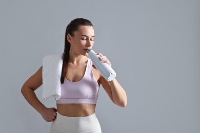 Photo of Woman in gym clothes drinking water on grey background, space for text