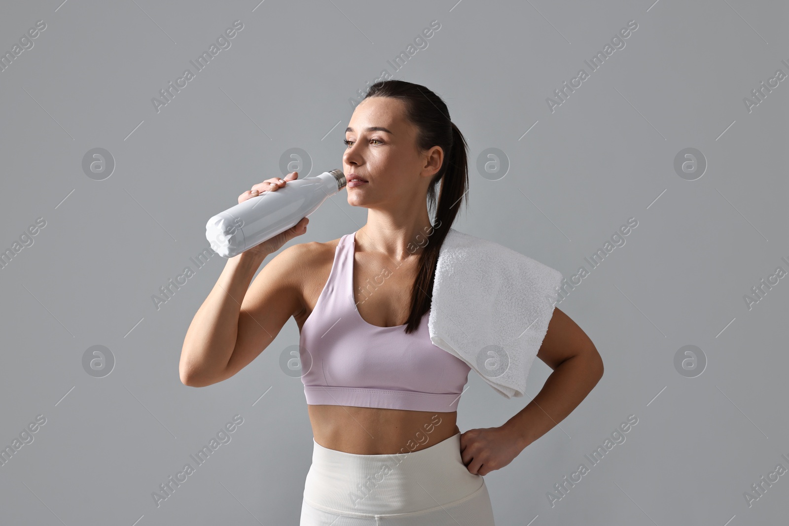 Photo of Woman in gym clothes drinking water on grey background