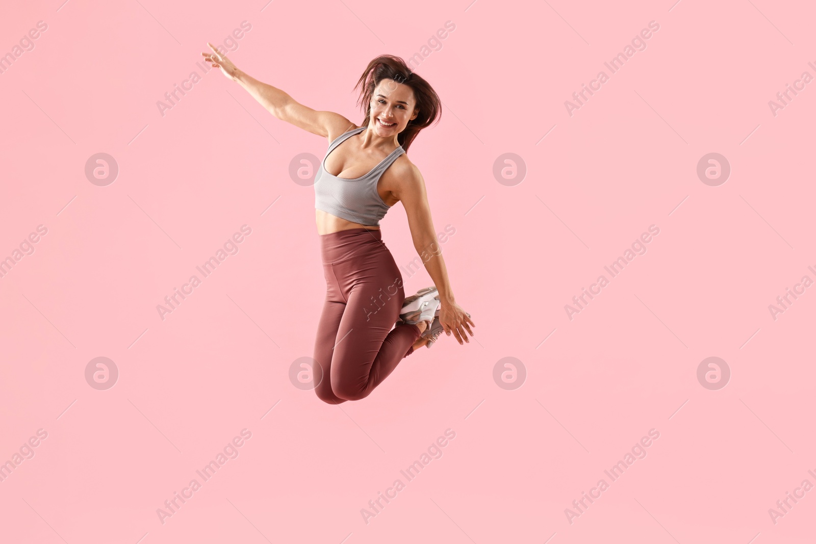 Photo of Woman in gym clothes jumping on pink background