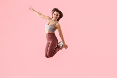 Photo of Woman in gym clothes jumping on pink background