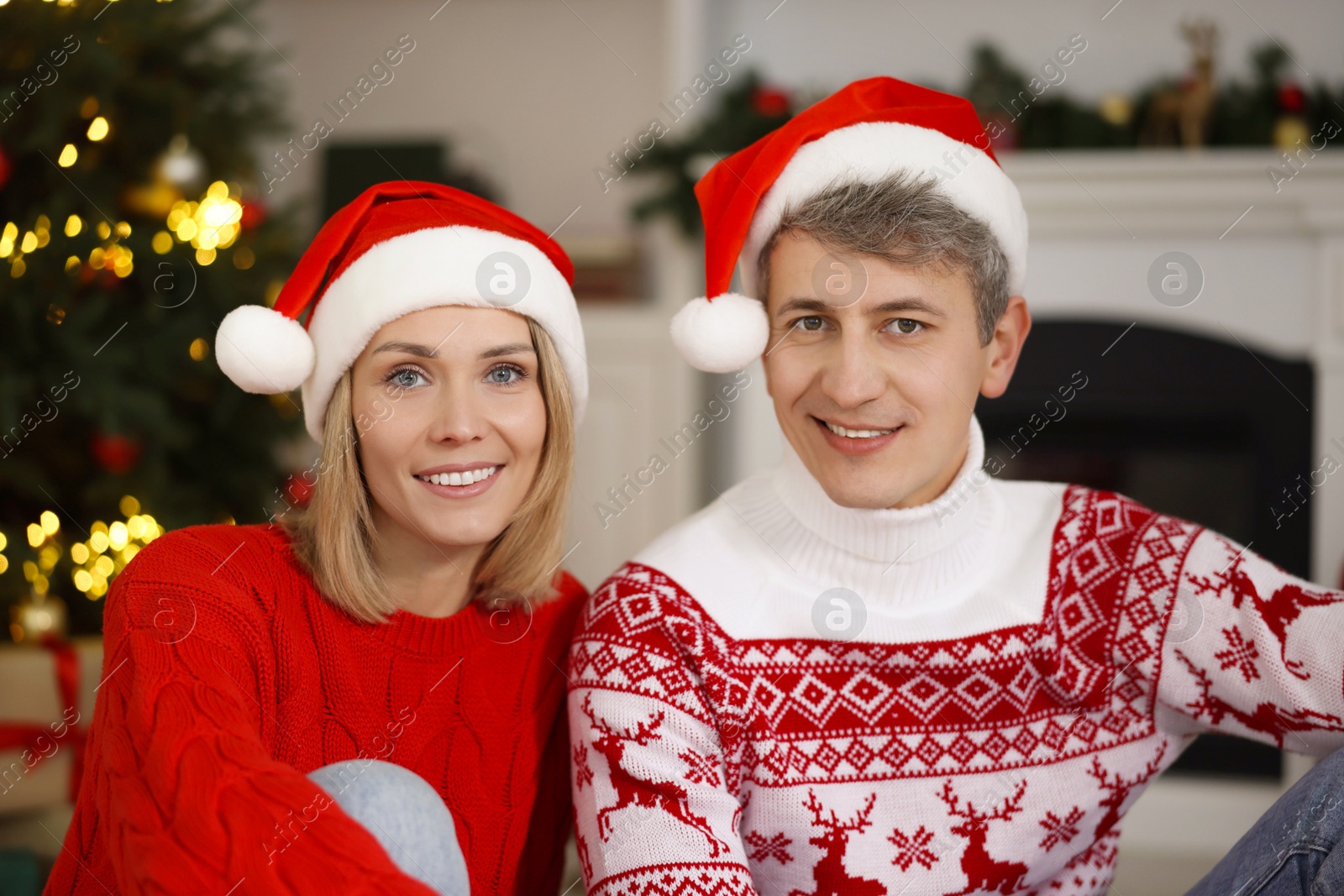 Photo of Lovely couple in Santa hats and Christmas sweaters at home