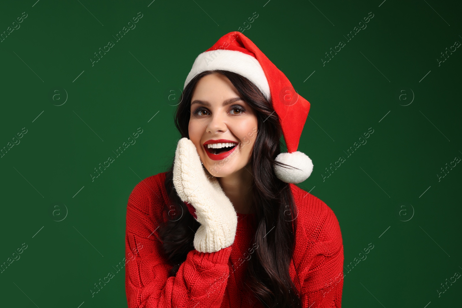 Photo of Attractive woman in Santa hat, sweater and mittens on green background. Christmas celebration