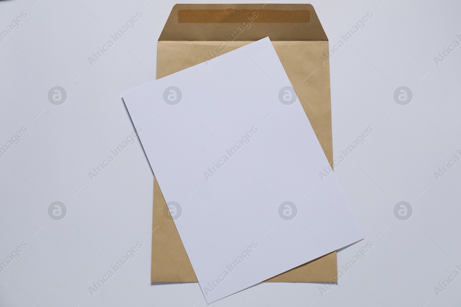 Photo of Kraft paper envelope with letter on white background, top view. Mockup for design