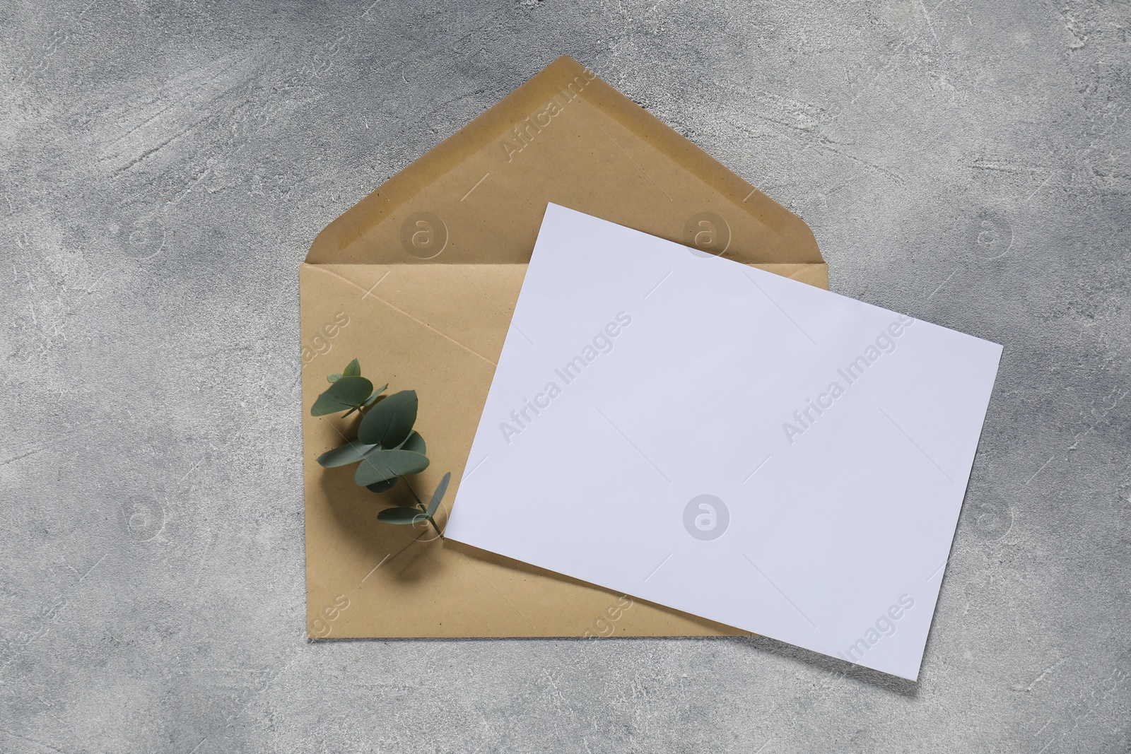 Photo of Kraft paper envelope with letter and eucalyptus branch on gray textured background, top view. Mockup for design