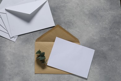 Photo of Paper envelopes with letter and eucalyptus branch on gray textured background, flat lay. Mockup for design