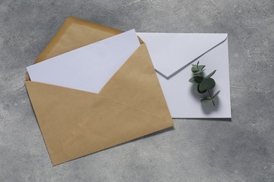 Photo of Paper envelopes with letter and eucalyptus branch on gray textured background, flat lay. Mockup for design