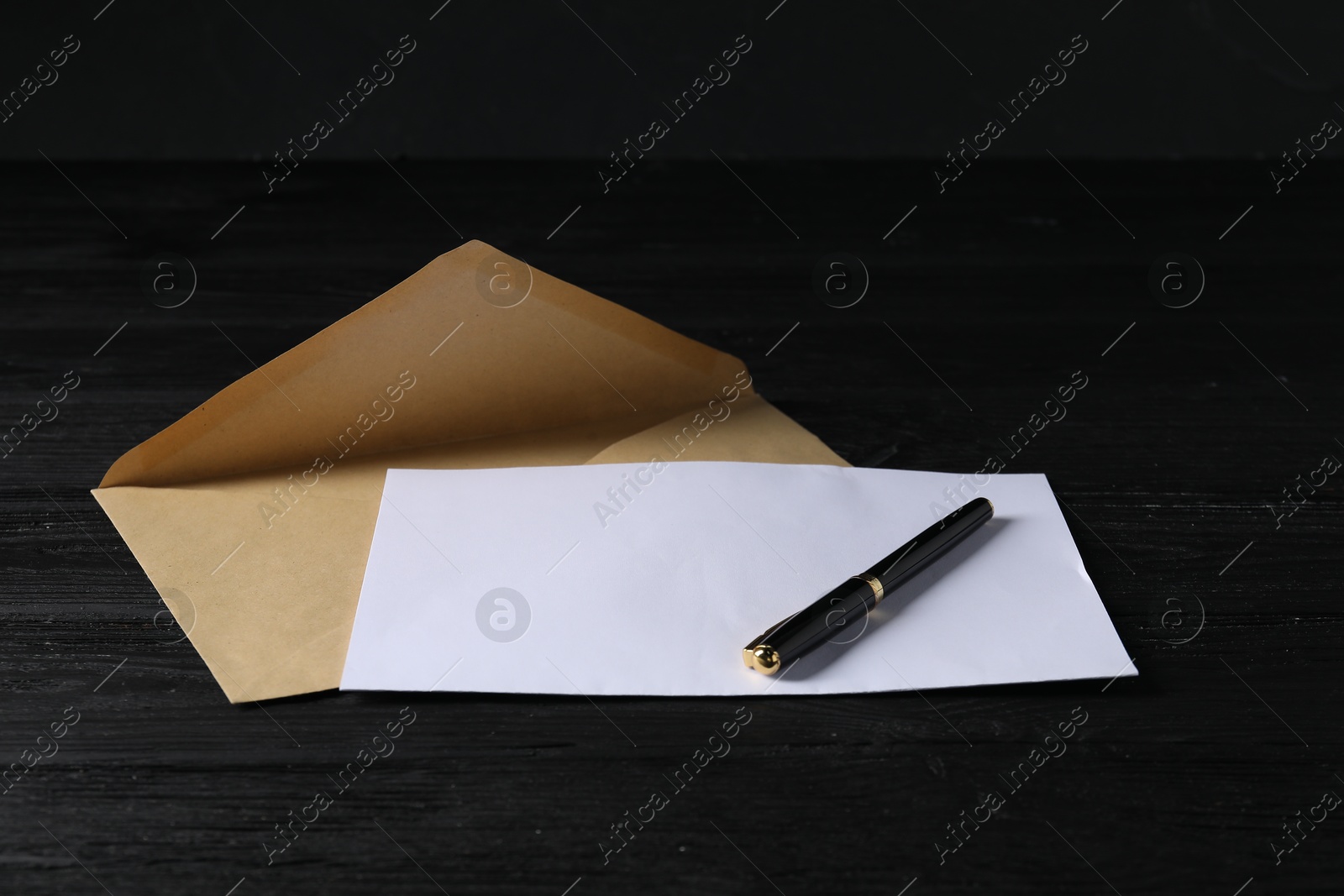 Photo of Kraft paper envelope with letter and pen on black wooden table. Mockup for design