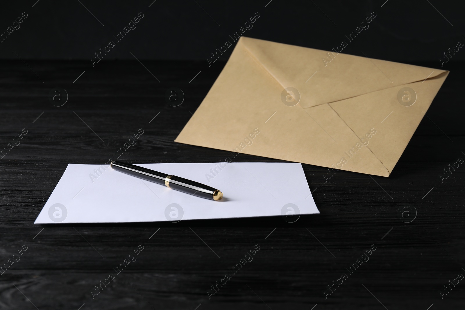 Photo of Kraft paper envelope with letter and pen on black wooden table. Mockup for design