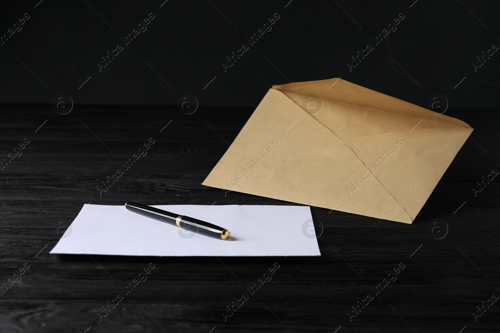 Photo of Kraft paper envelope with letter and pen on black wooden table. Mockup for design