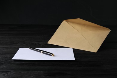 Photo of Kraft paper envelope with letter and pen on black wooden table. Mockup for design