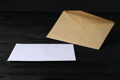 Photo of Kraft paper envelope with letter on black wooden table. Mockup for design