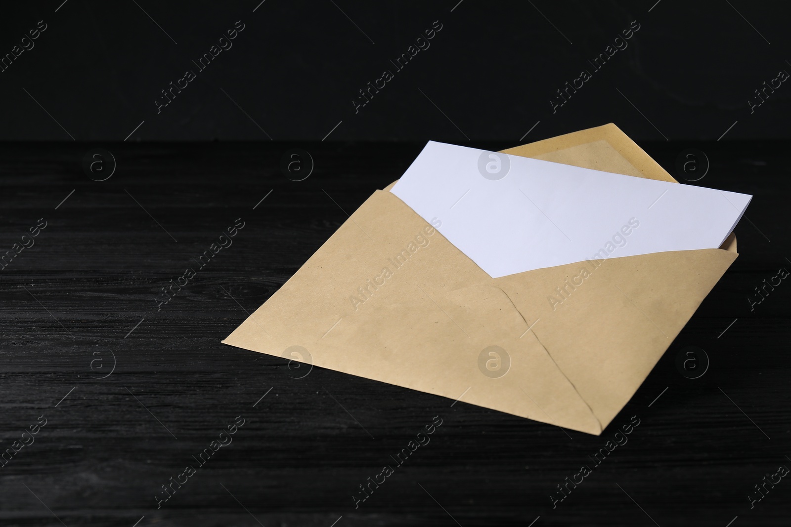 Photo of Kraft paper envelope with letter on black wooden table. Mockup for design