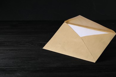 Photo of Kraft paper envelope with letter on black wooden table. Mockup for design