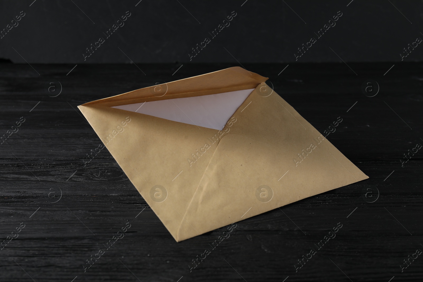 Photo of Kraft paper envelope with letter on black wooden table. Mockup for design