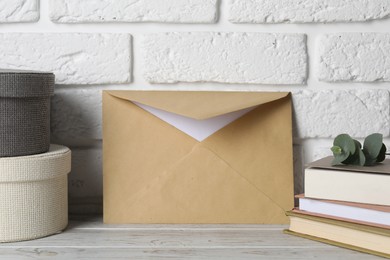 Photo of Kraft paper envelope with letter, boxes and books on wooden table near white brick wall. Mockup for design