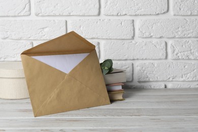 Photo of Kraft paper envelope with letter, books and eucalyptus branch on wooden table near white brick wall. Mockup for design