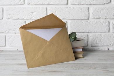 Photo of Kraft paper envelope with letter, books and eucalyptus branch on wooden table near white brick wall. Mockup for design