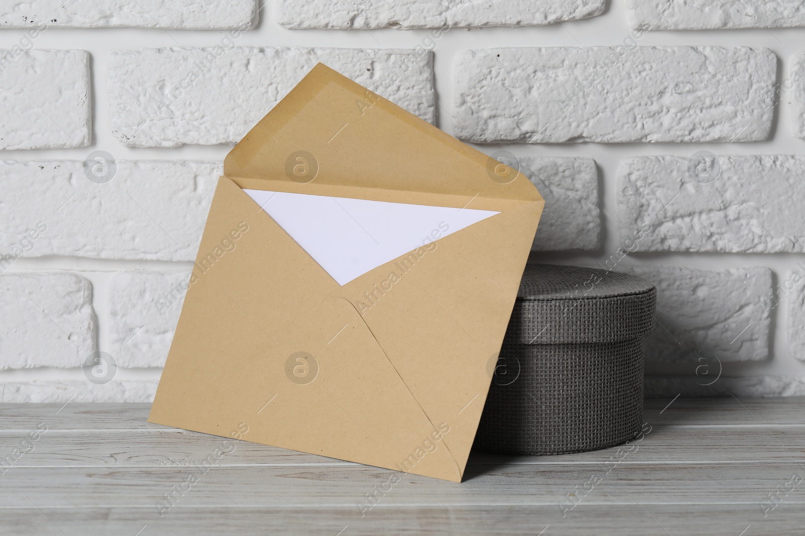 Photo of Kraft paper envelope with letter and box on wooden table near white brick wall. Mockup for design