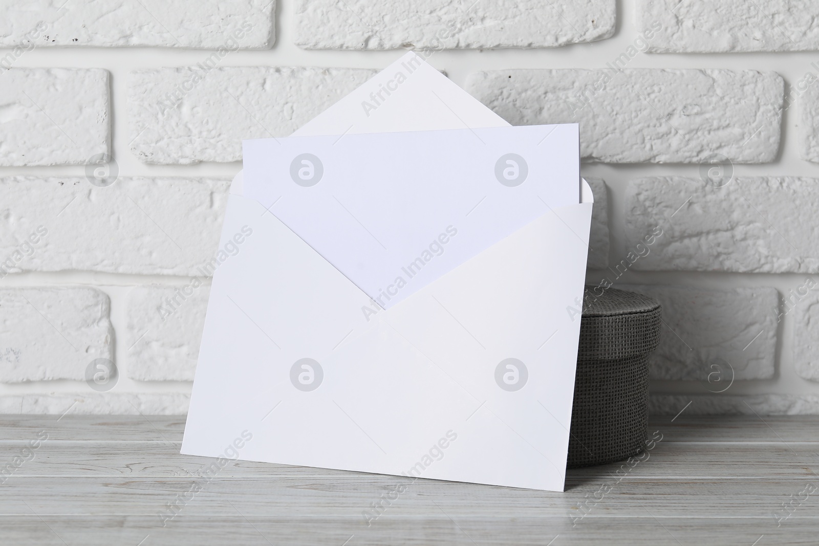 Photo of Paper envelope with letter on wooden table near white brick wall. Mockup for design