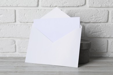 Photo of Paper envelope with letter on wooden table near white brick wall. Mockup for design