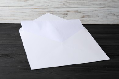 Photo of Paper envelope with letter on black wooden table. Mockup for design