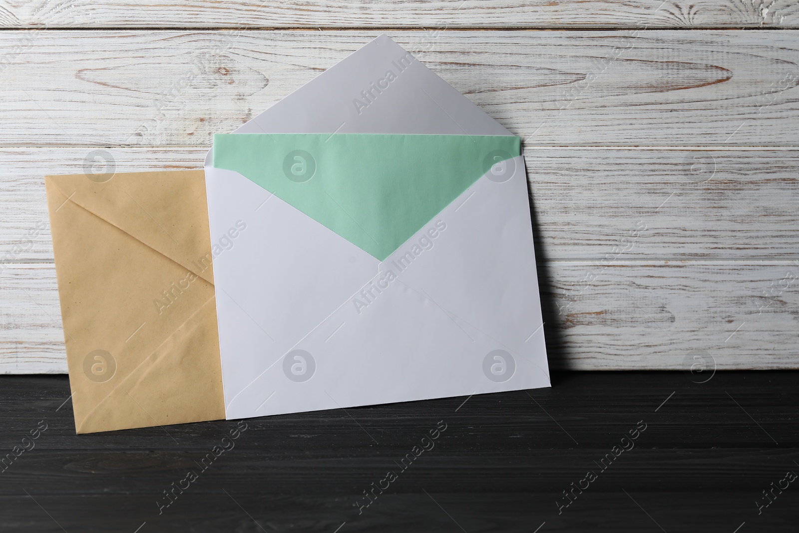 Photo of Paper envelopes with letter on black wooden table. Mockup for design