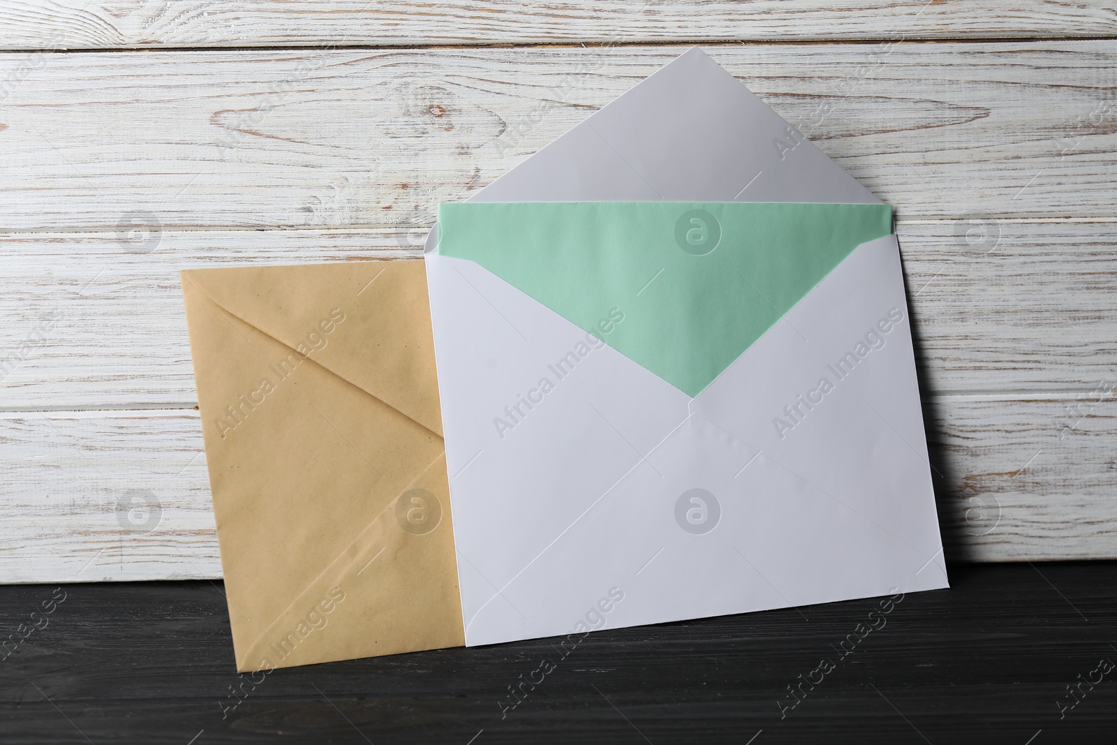 Photo of Paper envelopes with letter on black wooden table. Mockup for design