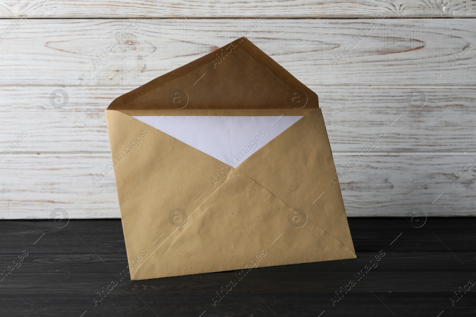 Photo of Kraft paper envelope with letter on black wooden table. Mockup for design