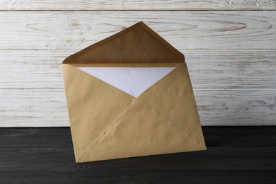 Photo of Kraft paper envelope with letter on black wooden table. Mockup for design