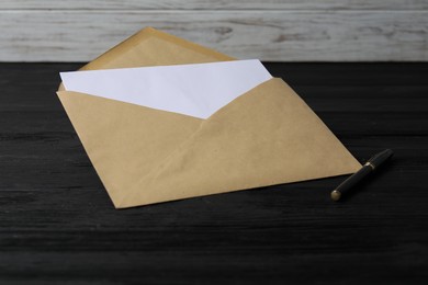 Photo of Kraft paper envelope with letter on black wooden table. Mockup for design