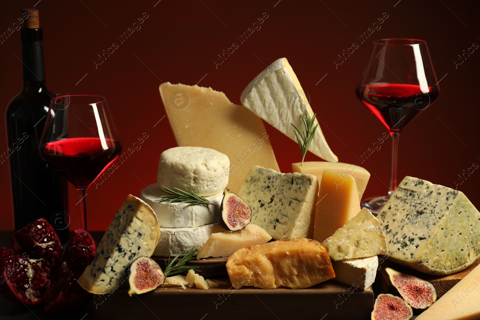 Photo of Different types of cheese, rosemary, figs, pomegranate and wine on table