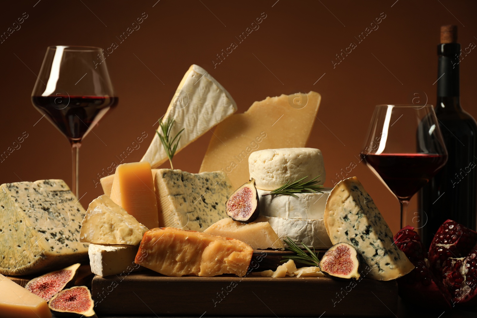 Photo of Different types of cheese, rosemary, figs, pomegranate and wine on table