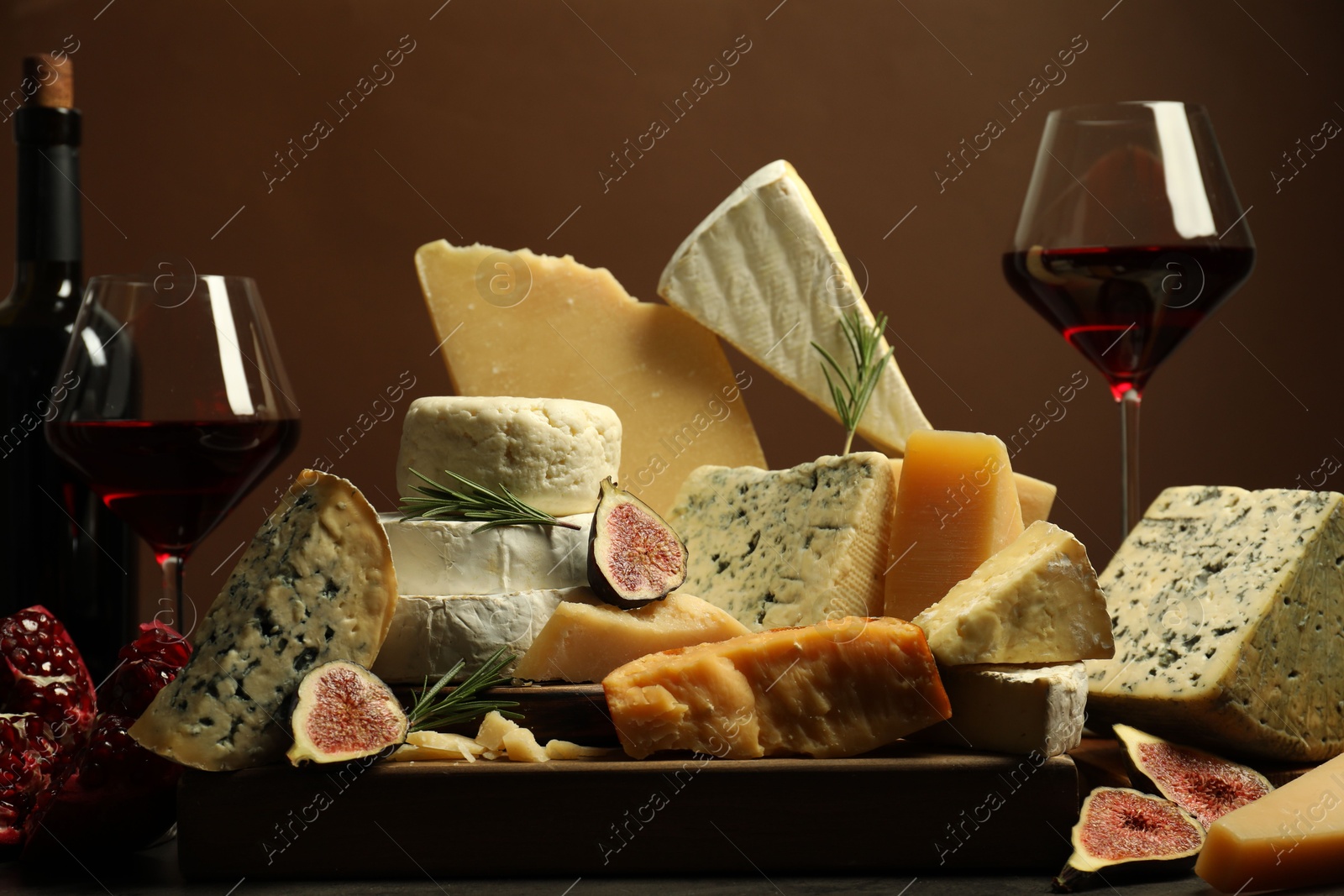 Photo of Different types of cheese, rosemary, figs, pomegranate and wine on table