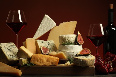 Photo of Different types of cheese, rosemary, figs, pomegranate and wine on table