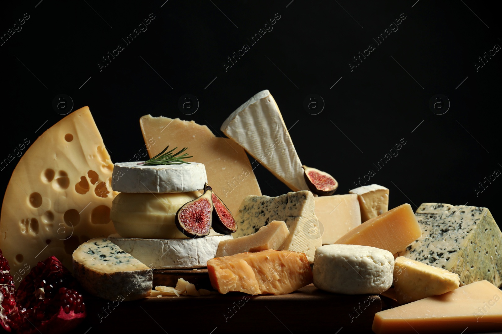 Photo of Different types of cheese, rosemary, figs and pomegranate on table