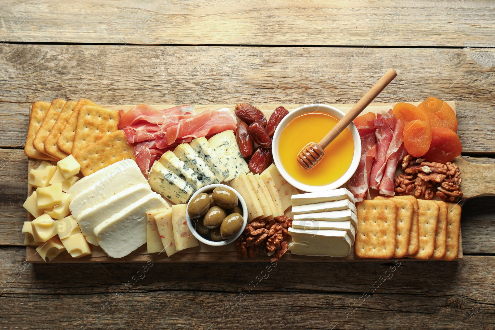 Photo of Different types of delicious cheese and other snacks on wooden table, top view