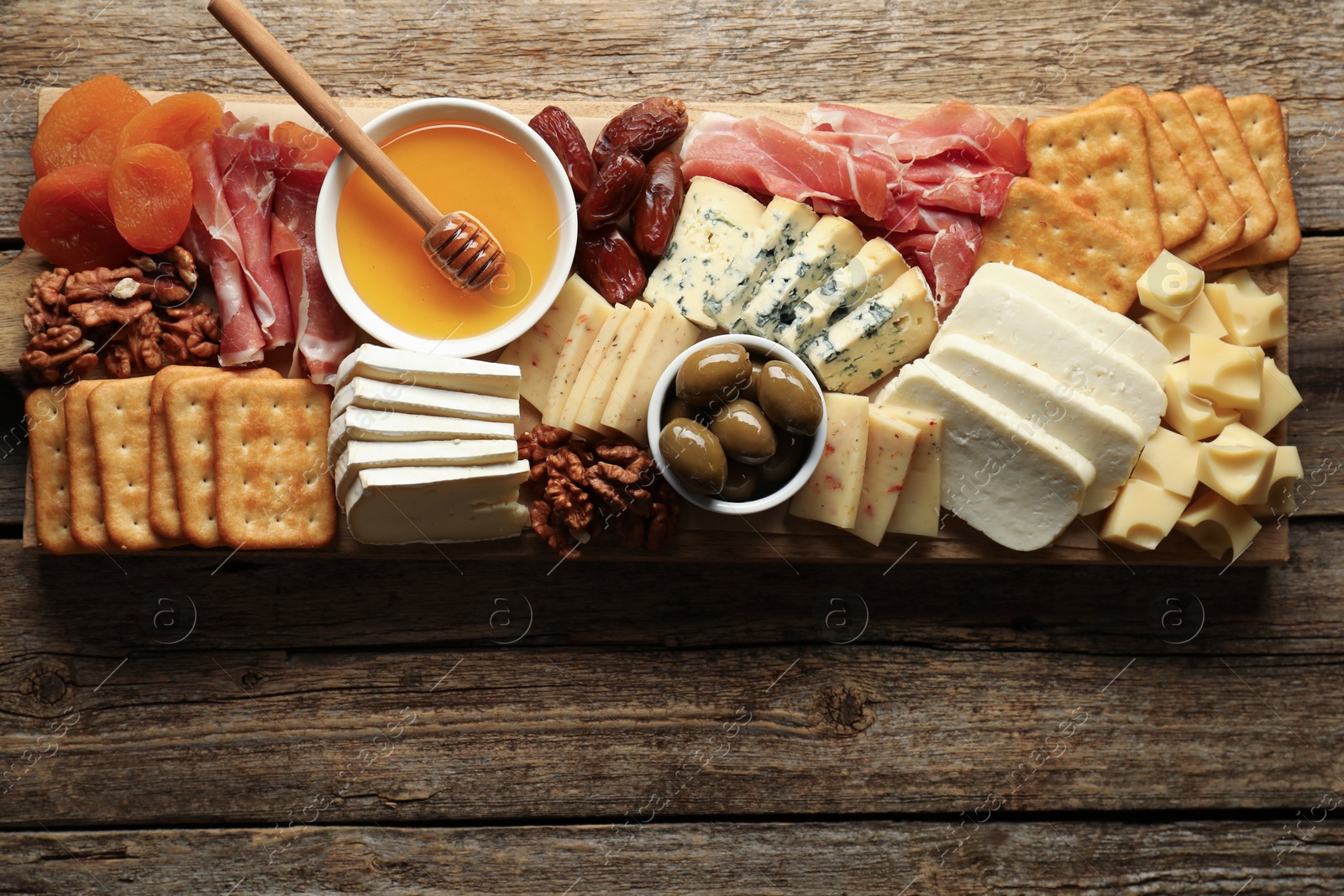 Photo of Different types of delicious cheese and other snacks on wooden table, top view. Space for text