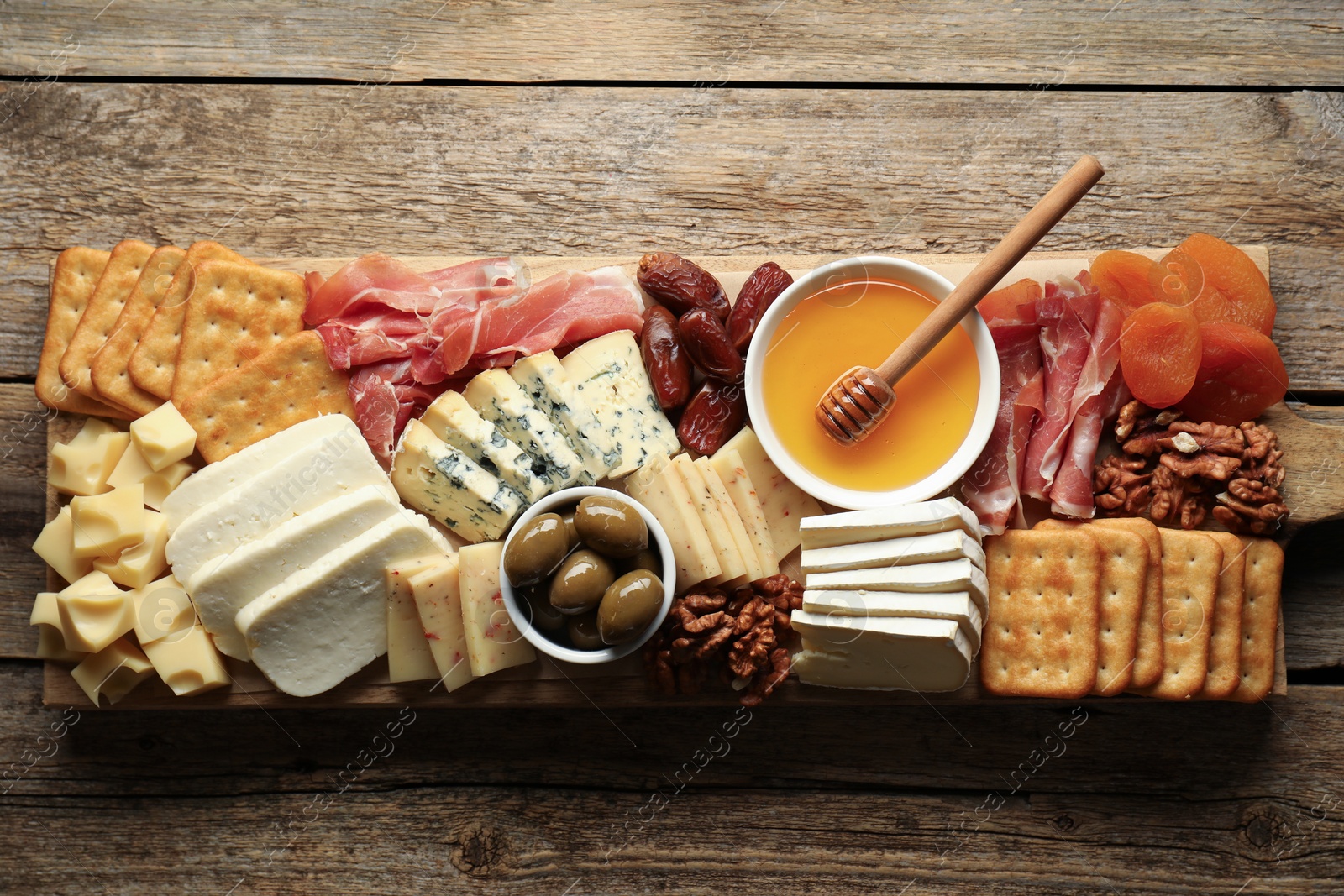 Photo of Different types of delicious cheese and other snacks on wooden table, top view