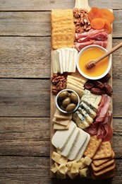 Photo of Different types of delicious cheese and other snacks on wooden table, top view