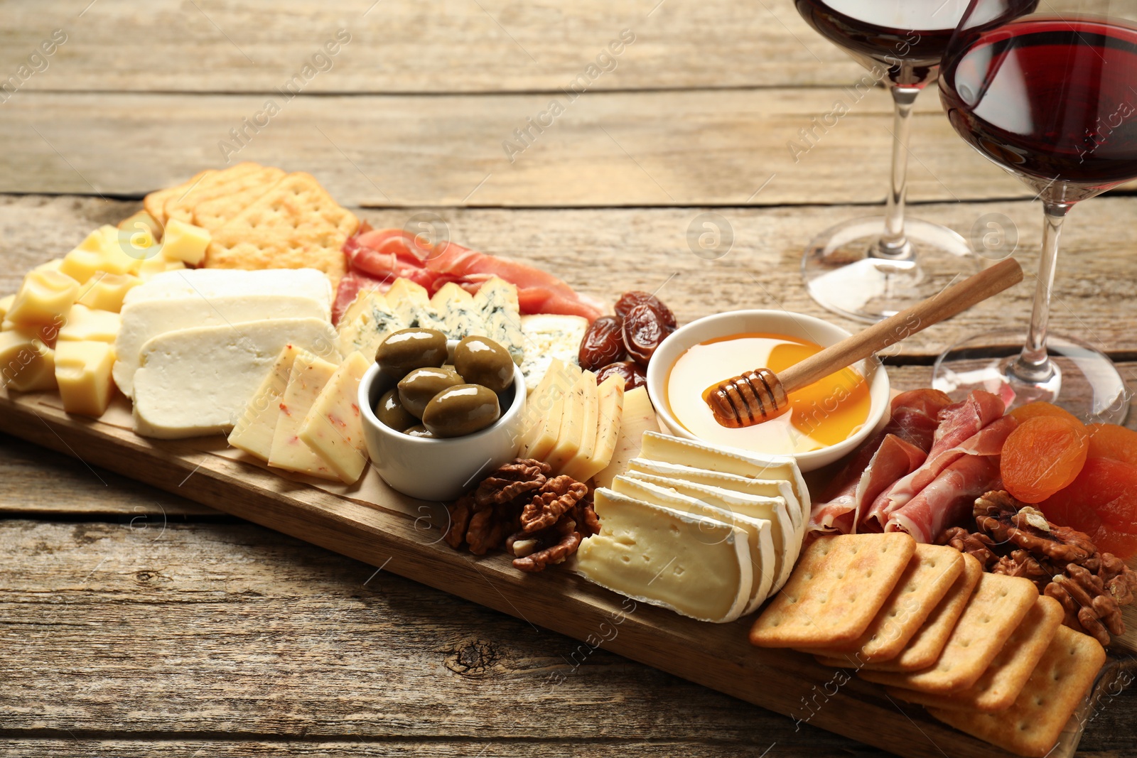 Photo of Different types of delicious cheese, other snacks and wine on wooden table, closeup