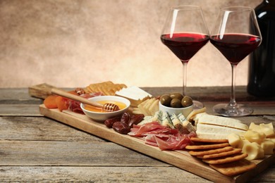 Photo of Different types of delicious cheese, other snacks and wine on wooden table, closeup